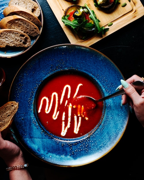Kobieta jedzenie zupa pomidorowa z roztopionym parmezanem wewnątrz niebieski talerz.