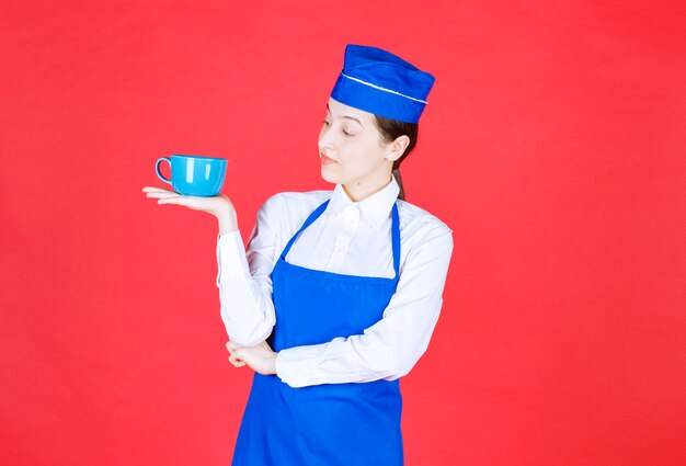 Kobieta kelnerka w mundurze stojąc i trzymając miskę na czerwonej ścianie.