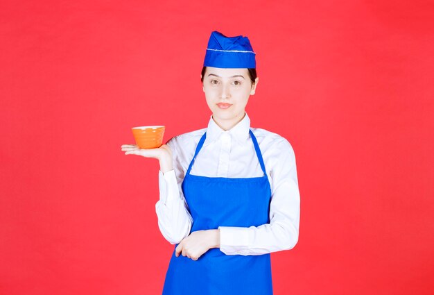 Kobieta kelnerka w mundurze stojąc i trzymając pomarańczową miskę.