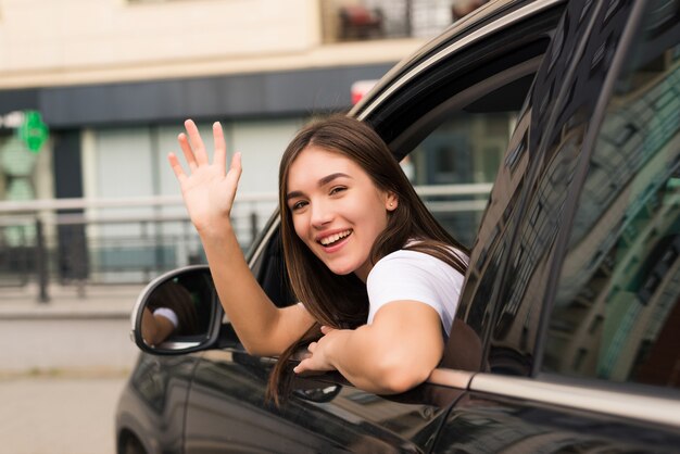 Kobieta kierowca samochodu macha na znak pożegnania na ulicy