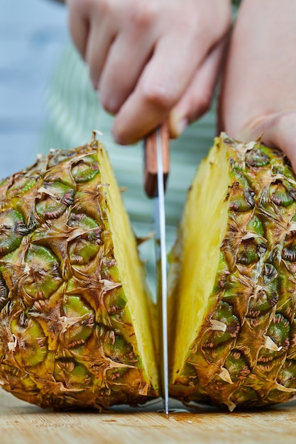 Kobieta kroi świeżego ananasa na drewnianej desce do krojenia, z bliska