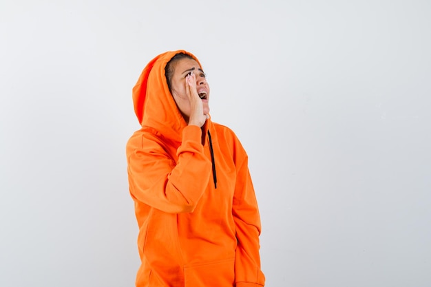 Kobieta krzycząca do kogoś w pomarańczowej bluzie z kapturem i wyglądająca na podekscytowaną
