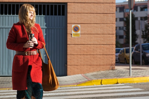 Bezpłatne zdjęcie kobieta krzyżuje ulicę z termosem