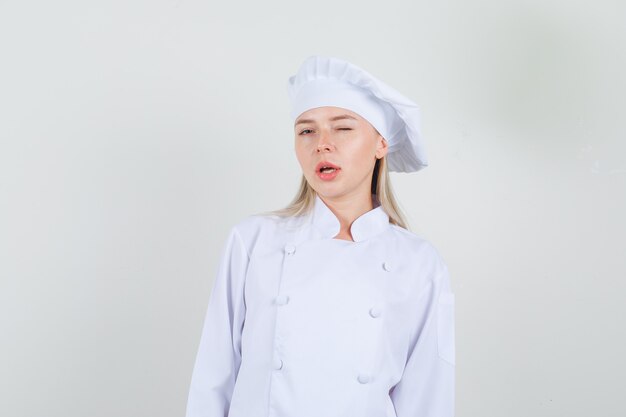 Kobieta kucharz mrugająca okiem w białym mundurze i wyglądająca na pewną siebie.