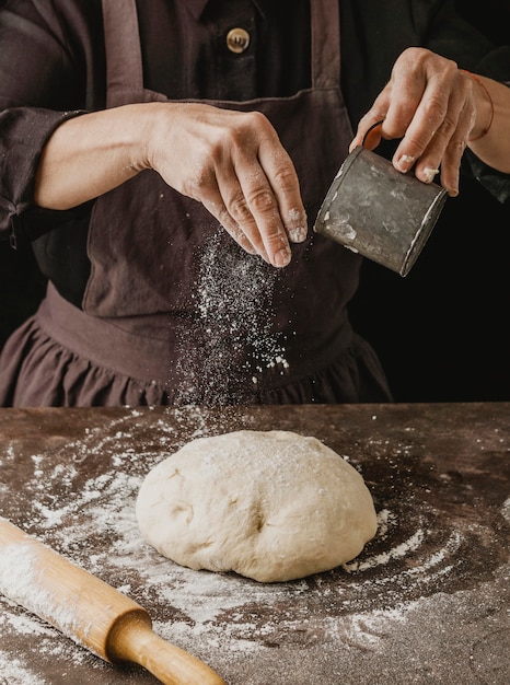 Kobieta kucharz odkurza mąkę na ciasto do pizzy