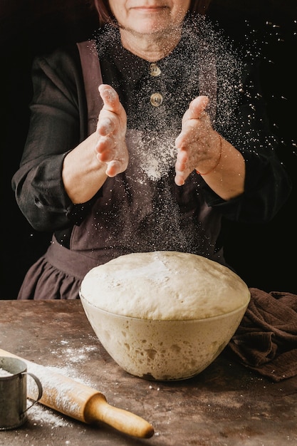 Kobieta kucharz odkurza ręce mąką przed przygotowaniem ciasta do pizzy