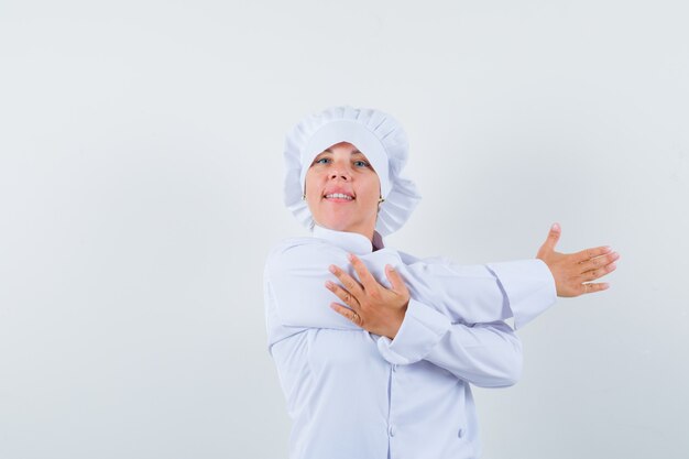 kobieta kucharz, rozciągając ramiona w białym mundurze i wyglądając na zrelaksowanego