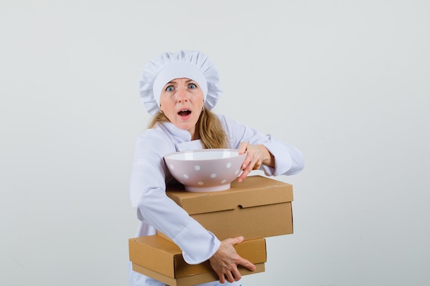 Bezpłatne zdjęcie kobieta kucharz trzyma miskę z kartonów w białym mundurze