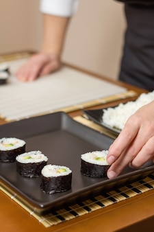 Kobieta kucharz umieszcza japońskie rolki sushi na tacy