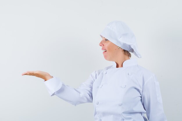 kobieta kucharz w białym mundurze patrząc na jej dłoń rozłożoną na bok i wyglądająca dumnie