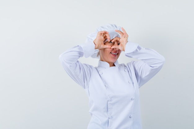 Bezpłatne zdjęcie kobieta kucharz w białym mundurze pokazując gest serca i patrząc zadowolony