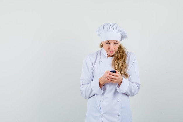 Kobieta kucharz w białym mundurze przy użyciu telefonu komórkowego i patrząc zajęty