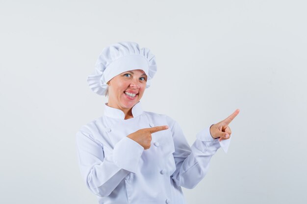 kobieta kucharz wskazując na bok w białym mundurze i patrząc wesoło.