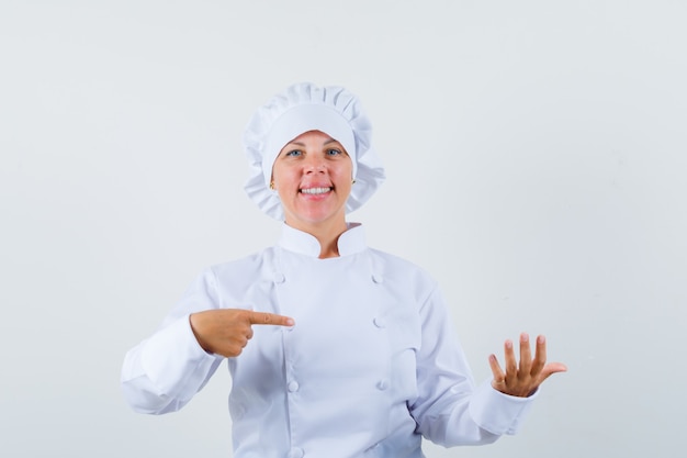 Kobieta kucharz wskazując na coś udawanego w białym mundurze i wyglądającą na pewną siebie
