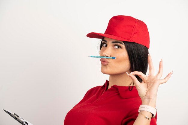 Kobieta kurier, trzymając pióro na ustach i pokazując znak ok. Wysokiej jakości zdjęcie