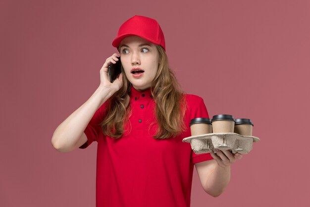 Kobieta Kurier W Czerwonym Mundurze Trzymając Kawę Rozmawia Przez Telefon Na Jasnoróżowym, Mundurze Służbowym Dostawa Usług Pracownika