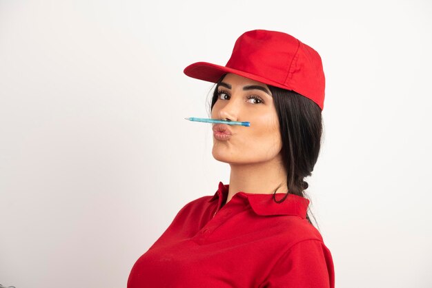 Kobieta kurier w czerwonym mundurze trzymając pióro na ustach. Wysokiej jakości zdjęcie