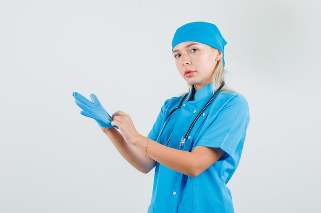 Kobieta lekarz nosi rękawiczki medyczne w niebieskim mundurze i wygląda poważnie