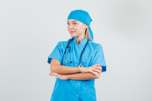 Bezpłatne zdjęcie kobieta lekarz patrząc na bok ze skrzyżowanymi rękami w niebieskim mundurze i patrząc z nadzieją.