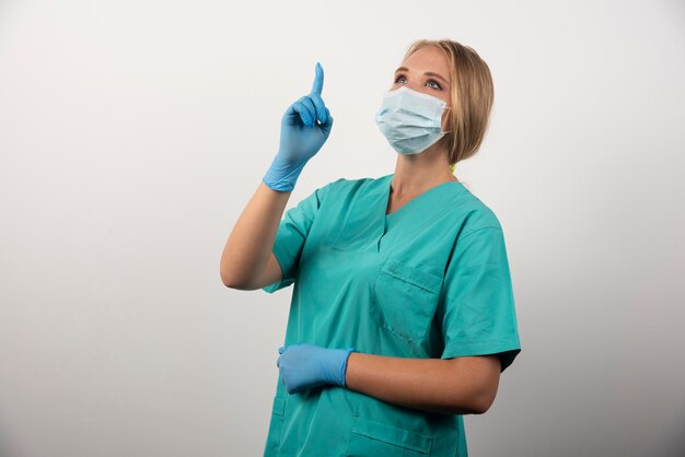 Kobieta lekarz pokazuje kciuk i noszenie maski medycznej.
