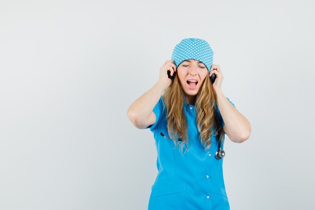 Kobieta lekarz słucha muzyki w słuchawkach w niebieskim mundurze i wygląda na zachwyconą