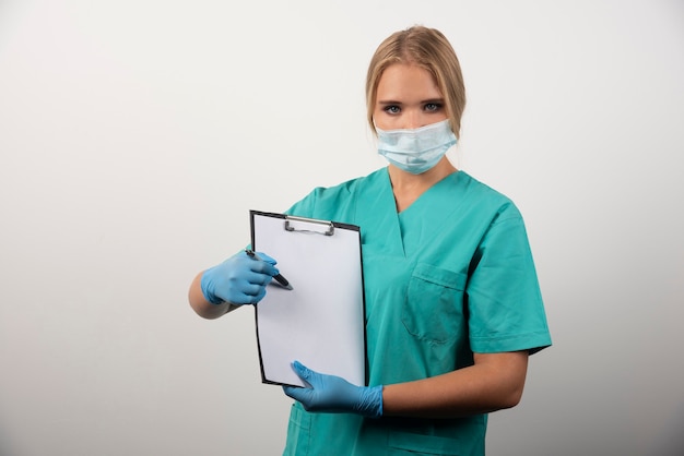 Kobieta lekarz trzymając schowek i noszenie maski medycznej.