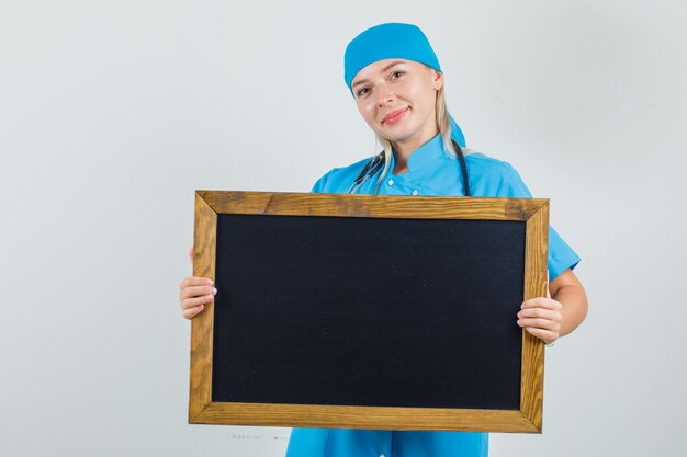 Kobieta lekarz trzymając tablicę i uśmiechając się w niebieskim mundurze