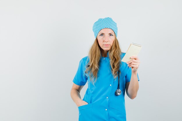 Kobieta lekarz trzymając zeszyt ręką w kieszeni w niebieskim mundurze