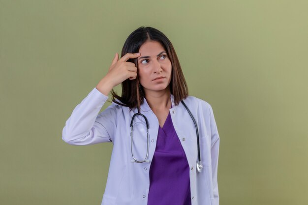 kobieta lekarz ubrany w biały fartuch i stojąc z stetoskopem palcem przed myśleniem świątynnym próbuje dokonać wyboru na odizolowanej zieleni