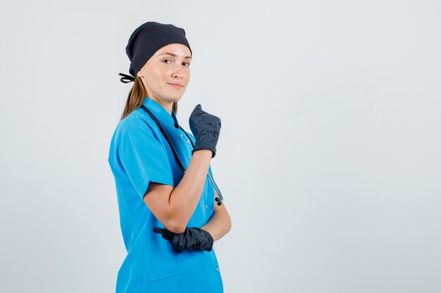 Kobieta lekarz w mundurze, rękawiczki pozowanie, trzymając podniesioną pięść i wyglądając pewnie.