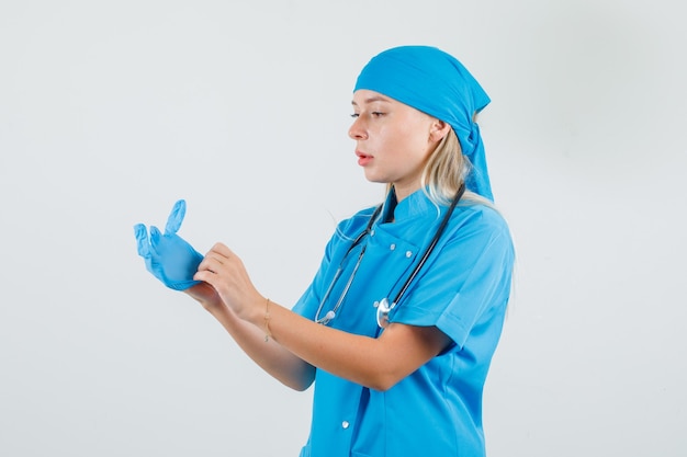 Kobieta lekarz w rękawiczkach medycznych w niebieskim mundurze i patrząc ostrożnie.