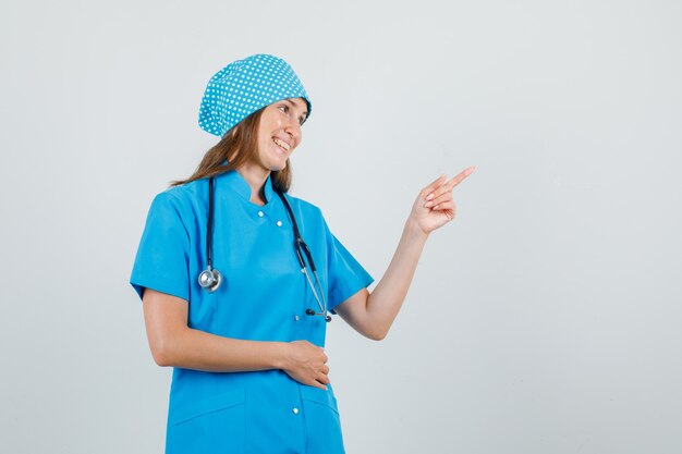 Kobieta lekarz wskazując i patrząc z boku w niebieskim mundurze i patrząc wesoło