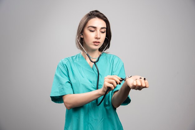Kobieta lekarz z stetoskopem sprawdzanie siebie na szarej ścianie.