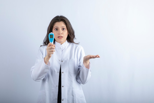 Kobieta lekarz z termometrem stojąc na białej ścianie.