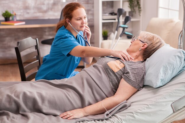 Kobieta lekarz za pomocą stetoskopu, aby sprawdzić serce staruszki w domu opieki.
