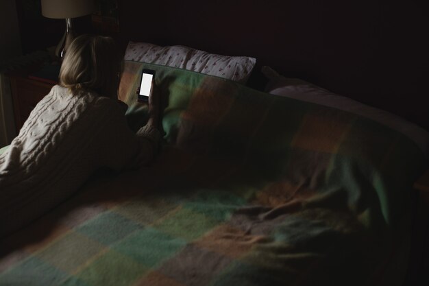 Kobieta leży i przy użyciu telefonu komórkowego na łóżku