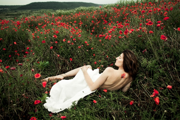 Bezpłatne zdjęcie kobieta leży nago w białej koszuli wśród kwiatów maku
