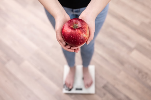 Kobieta mierzy wagę na wadze, trzyma w rękach jabłko.