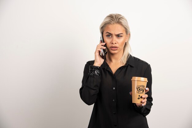 Kobieta mówi na telefon komórkowy i trzyma filiżankę kawy. Wysokiej jakości zdjęcie