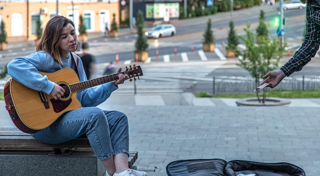 Kobieta muzyk gra na gitarze akustycznej i śpiewa na zewnątrz na ulicy