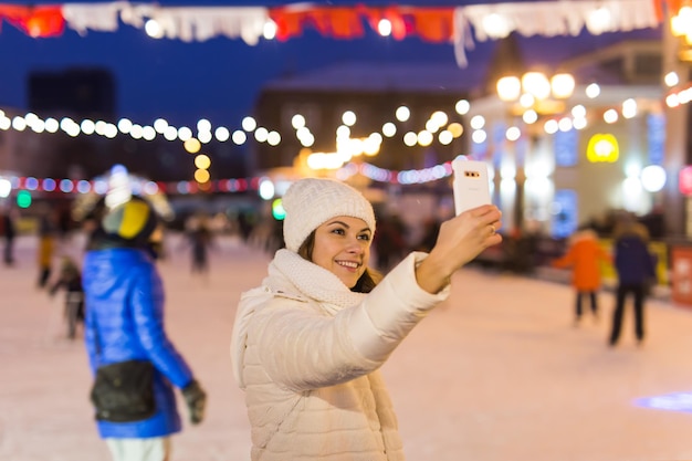 Kobieta na lodowisku jeździ na łyżwach i robi selfie na smartfonie sylwestra i wróżka bożonarodzeniowa