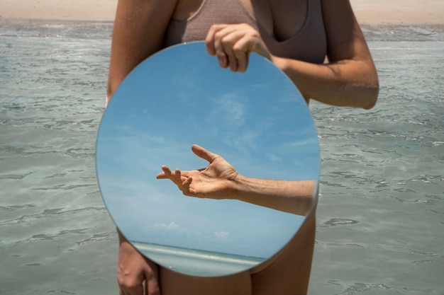 Kobieta na plaży latem pozuje z okrągłym lustrem