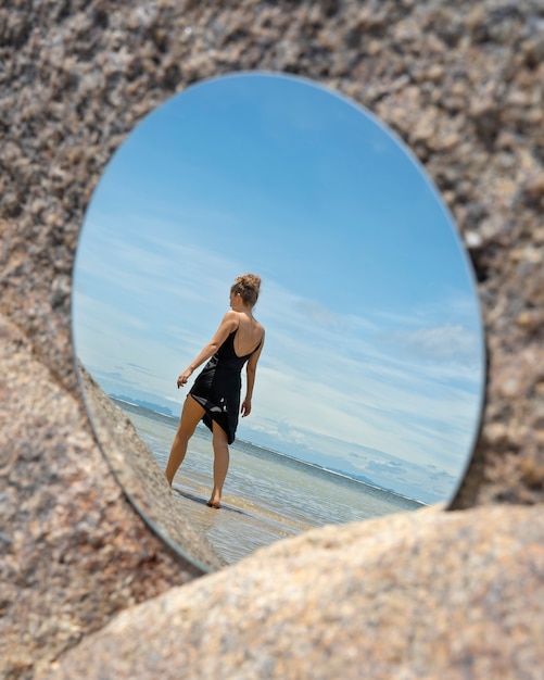 Kobieta na plaży latem pozuje z okrągłym lustrem