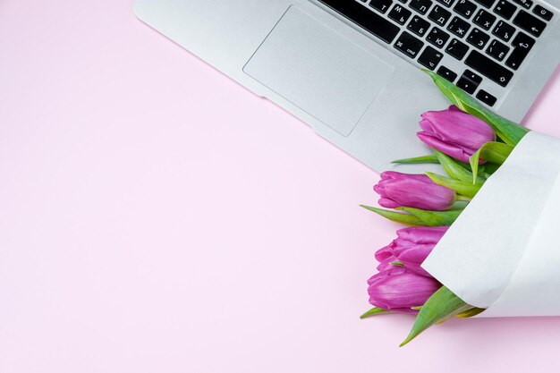 Kobieta na pulpicie z laptopem i fioletowymi tulipanami na różowym tle Płaskie świeckie wiosenne wakacje Dzień matki