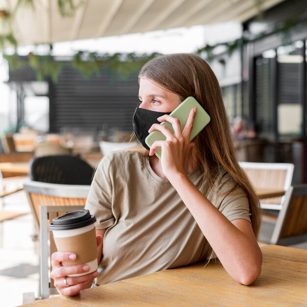 Kobieta na tarasie z maską rozmawia przez telefon komórkowy