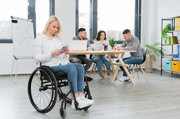 Kobieta na wózku inwalidzkim pracuje od jej telefonu przy biurem