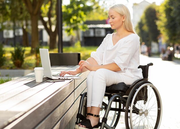 Kobieta na wózku inwalidzkim za pomocą laptopa na zewnątrz