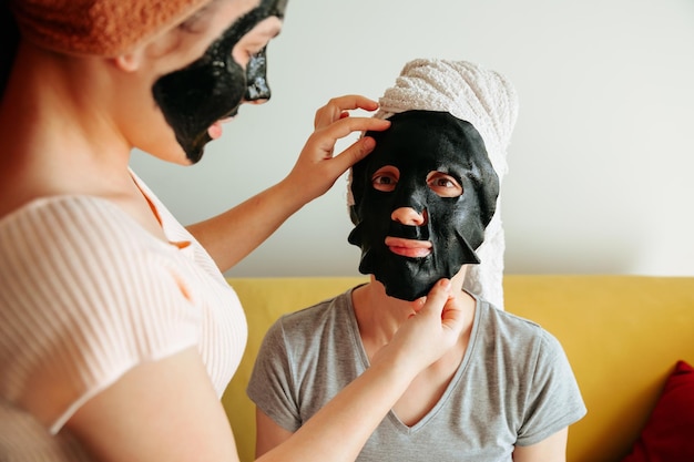 Kobieta nakłada papierową czarną maskę pielęgnacja skóry zabiegi kosmetyczne maska do pielęgnacji skóry kobieta młody salon spa