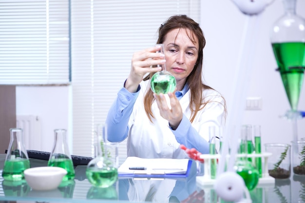 Kobieta naukowiec patrząca z wielką uwagą na zielone rozwiązanie. Laboratorium badawcze.