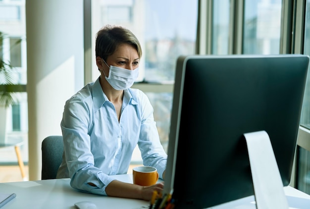 Kobieta nosząca maskę podczas pracy na komputerze stacjonarnym w biurze